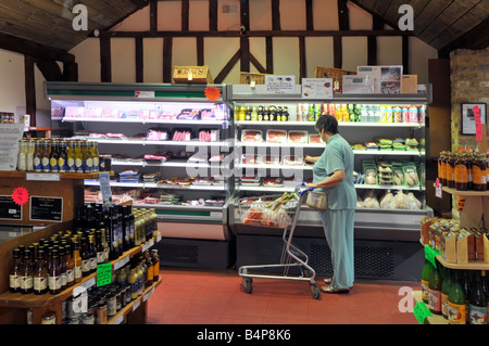 Interior of retail farm shop produce on display woman shopping with supermarket trolley Stock Photo