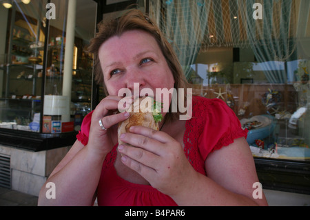 Overweight woman eating a large roll Stock Photo