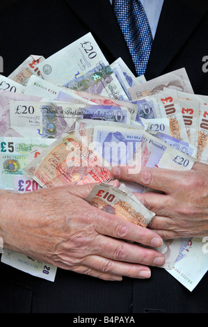 Smart man wearing office business suit with hands clutching piles of money concept for bankers, fatcats, greed, Men in Suits England UK Stock Photo