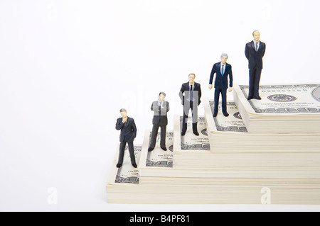 Male figurines standing on different levels of stack of dollars Stock Photo