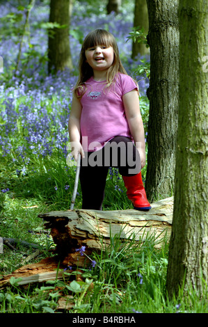 A girl standing with one foot on a fallen tree in a bluebell wood Stock Photo