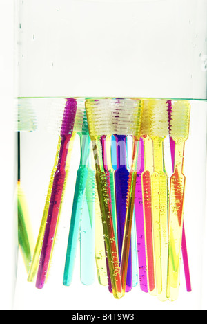 close up of submerged and floating brightly coloured toothbrushes in glass vase Stock Photo