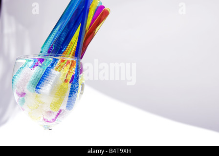 wine glass filled with fizzy water and multicoloured toothbrushes shot from side with curved shadow and white backdrop Stock Photo