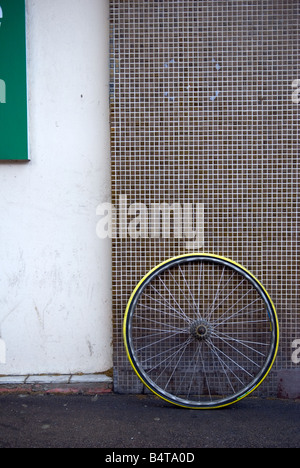 abandoned defunct yellow racing bike wheel leaning against tiled wall Stock Photo