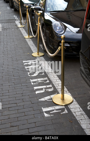 looking down at the word 'reserve' stencilled on the road next to parked luxury cars cordoned off in front of classy hotel Stock Photo