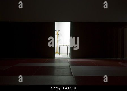 looking across a dark gym to an open door of brightly light room with empty coat stand and table Stock Photo