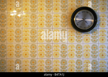 a clock hangs alone on a flowered tiled wall from sixties in kitchen Stock Photo