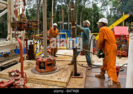 Remote jungle rainforest onshore oil and gas rig site with workers lifting sub connector for pipe with chain tong, Gabon, Africa Stock Photo