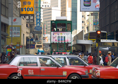 A traditional old tram travelling through the Wan Chai area of Hong Kong Island with familiar red taxi's in the foreground. Stock Photo