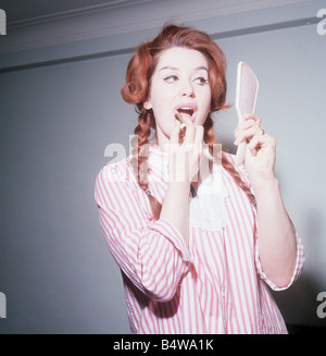 Heller Toren model actress 1964 puting on lipstick holding hand mirror pink striped shirt Stock Photo