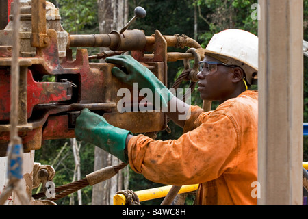 Oil rig crewman at work on rig floor of onshore oil and gas rig site in rainforest, Gabon, Africa Stock Photo