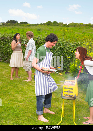 Young man tending barbecue with friends Stock Photo