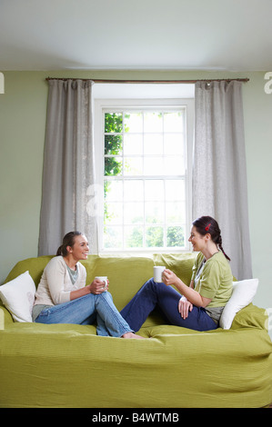 Two young women on couch, with mugs Stock Photo