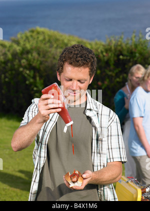 Man pouring ketchup onto hot dog Stock Photo