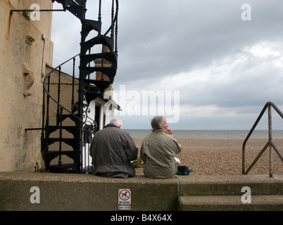 Elderly couple eating chips looking out to sea. Stock Photo