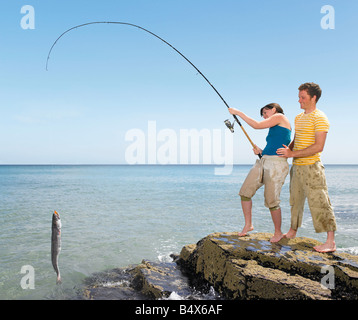 Couple landing a big fish off rocks Stock Photo