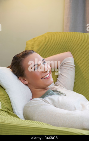 Smiling young woman lying on couch Stock Photo