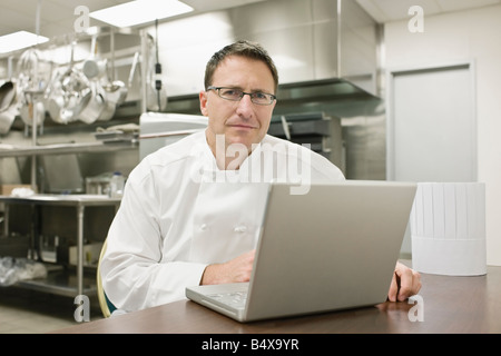 Chef working on laptop in kitchen Stock Photo