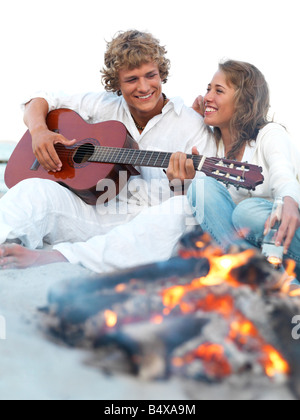 Young couple relaxing by campfire on beach Stock Photo