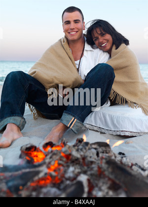 Young couple relaxing by campfire on beach Stock Photo