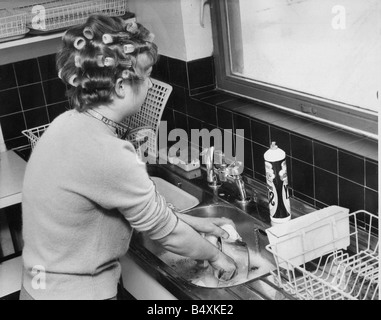 A woman is doing the washing up whislt waiting for her hair to curl before a night on the town Stock Photo