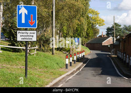 Single carriageway narrow road with sign that says priority over oncoming vehicles Stock Photo