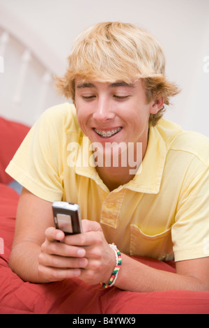 Teenage Boy Lying On Bed Using Mobile Phone Stock Photo