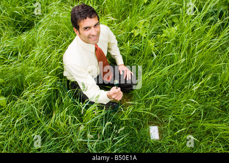 A mixed ethnicity businessman holding the plug end of an extension cord next to an electrical outlet in the ground in a grassy f Stock Photo