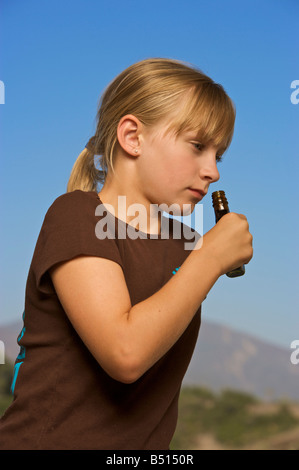 Young girl smelling a small bottle with blue sky background Stock Photo