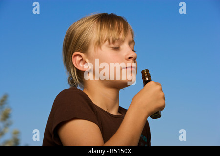 Young girl smelling a small bottle with blue sky background Stock Photo