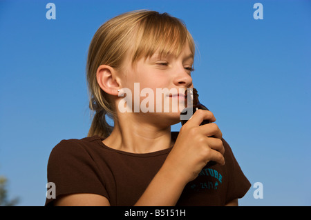 Young girl smelling a small bottle with blue sky background Stock Photo