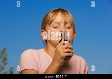 Young girl smelling a small bottle with blue sky background Stock Photo