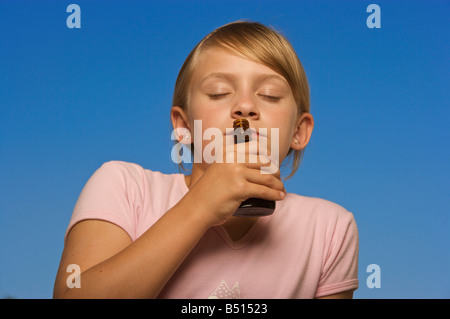 Young girl smelling a small bottle with blue sky background Stock Photo