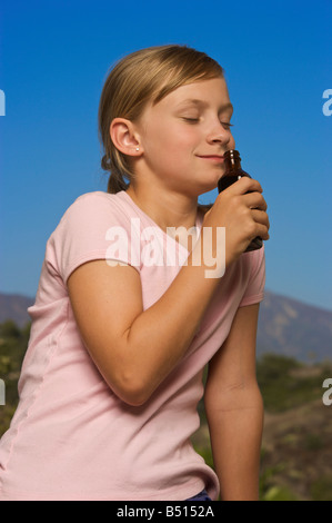 Young girl smelling a small bottle with blue sky background Stock Photo