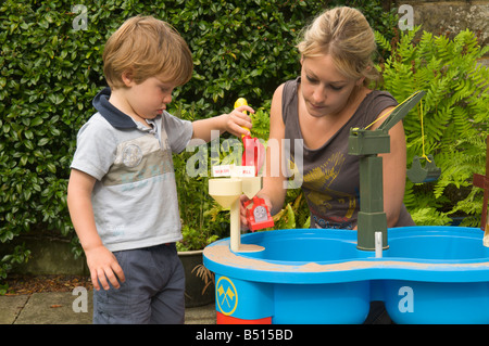 young child boy playing outside with his mother at a sand pit with measuring tools Stock Photo