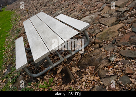 Metal picnic table setting on a rock surface by the edge of a road in a park Stock Photo