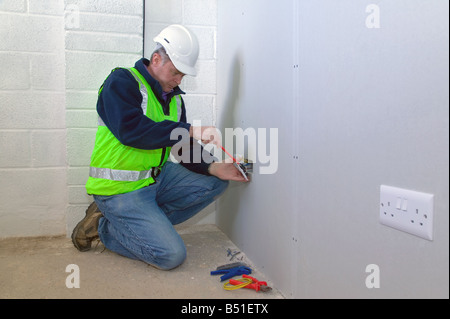 An electrician wearing safety clothing installing an electrical socket Stock Photo