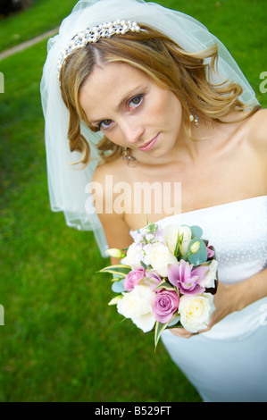 Bride holding floral bouquet in church garden looking up at camera Stock Photo