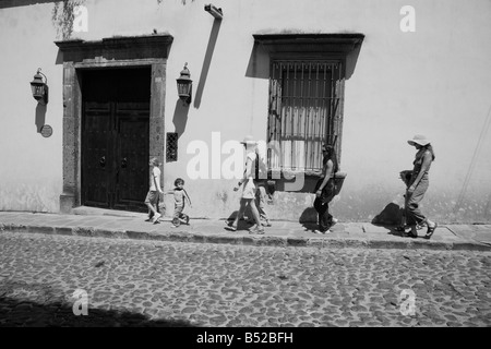 Families vacationing with young children stroll down a sidewalk in small Mexican colonial town Stock Photo