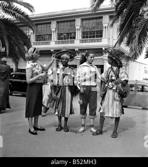 French actresses buy a drink of water from a local vendor in the town of Marrakech during their visit to Morocco. December 1952 Stock Photo