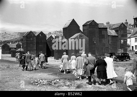 Holiday scenes. in and around Hastings.. Tourist walk along the seafront past the wooden sheds that holding the fishing nets of Stock Photo