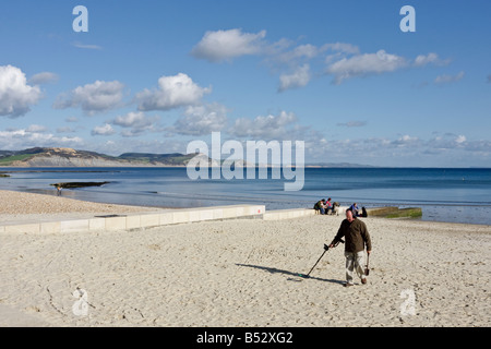 Beachcomber with Metal detector searches the beach at Lyme Regis Dorset on white sand with blue sky. Series of 5 Stock Photo