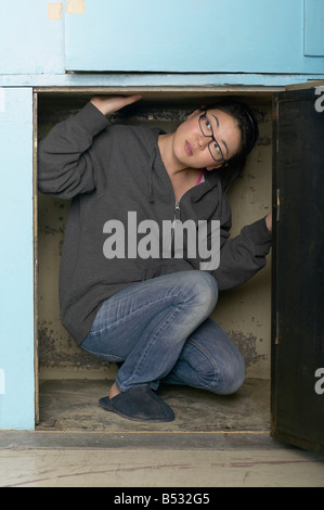 Mixed race woman crouching in small space Stock Photo