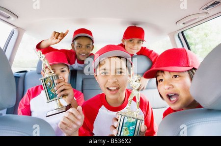 Multi-ethnic boys in car wearing baseball uniforms and holding trophies Stock Photo