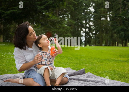 Boy blowing bubbles in park with mother Stock Photo