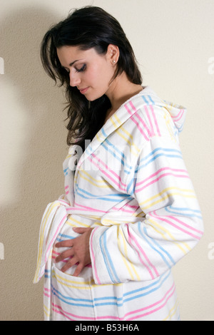 young pregnant woman in dressing gown looking down at her bump Stock Photo