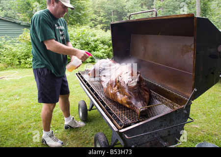 Picnic chef sprays roasting pig with apple cider to keep the pig juicy on a 4th of July pig roast in western Massachusetts Stock Photo