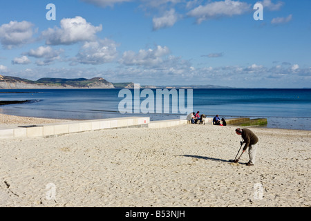 Beachcomber with Metal detector searches the beach at Lyme Regis Dorset on white sand with blue sky. Series of 5 Stock Photo