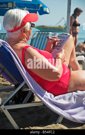 Senior woman sitting on lounge chair doing a crossword puzzle Stock Photo