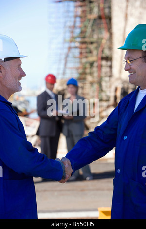 Two construction engineers shaking hands with colleagues standing behind them Stock Photo